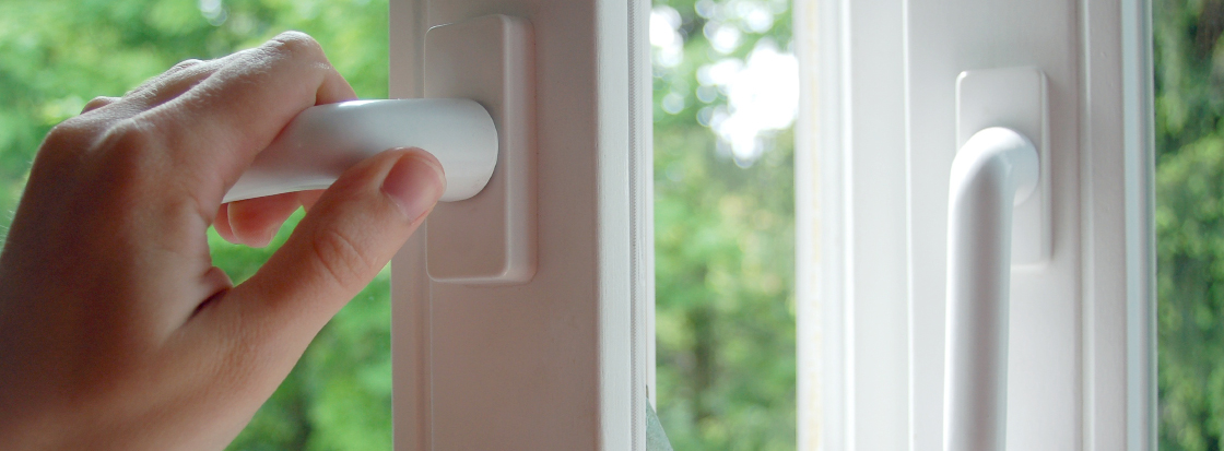 Das Foto zeigt eine Hand, die ein Fenster zum Stoßlüften oder allgemeinem Lüften öffnet, was der Bildung von Schimmel in Innenräumen vorbeugen kann.