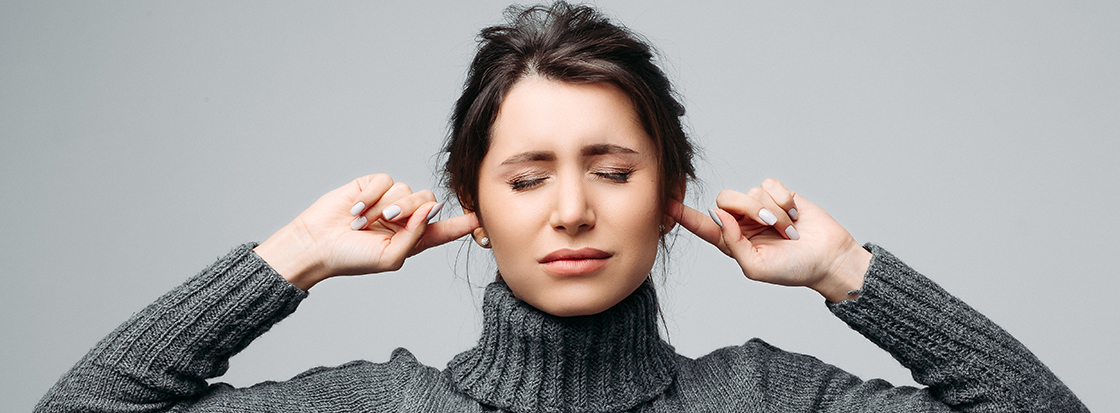 Das Foto zeigt das Portrait einer frau, die sich mit ihren Fingern die Ohren zuhält, um eien Störgeräusch nicht hören zu müssen.