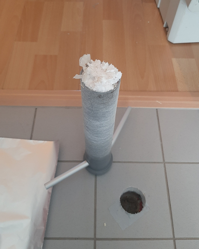 Zu sehen ist ein Bohrkern zur Untersuchung der Estrichdämmung und das Bohrloch im Fliesenboden, welches dazu angelegt wurde.